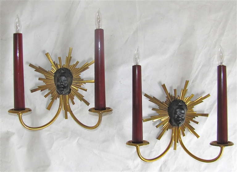 Pair of French Napoleon III style two light brass and black patinated wall sconces with soleil and Nubian motif. Dark red painted wood tapered candle sleeves. Each sconce uses 2 -  40 watt max candalabra base bulbs. Newly wired.