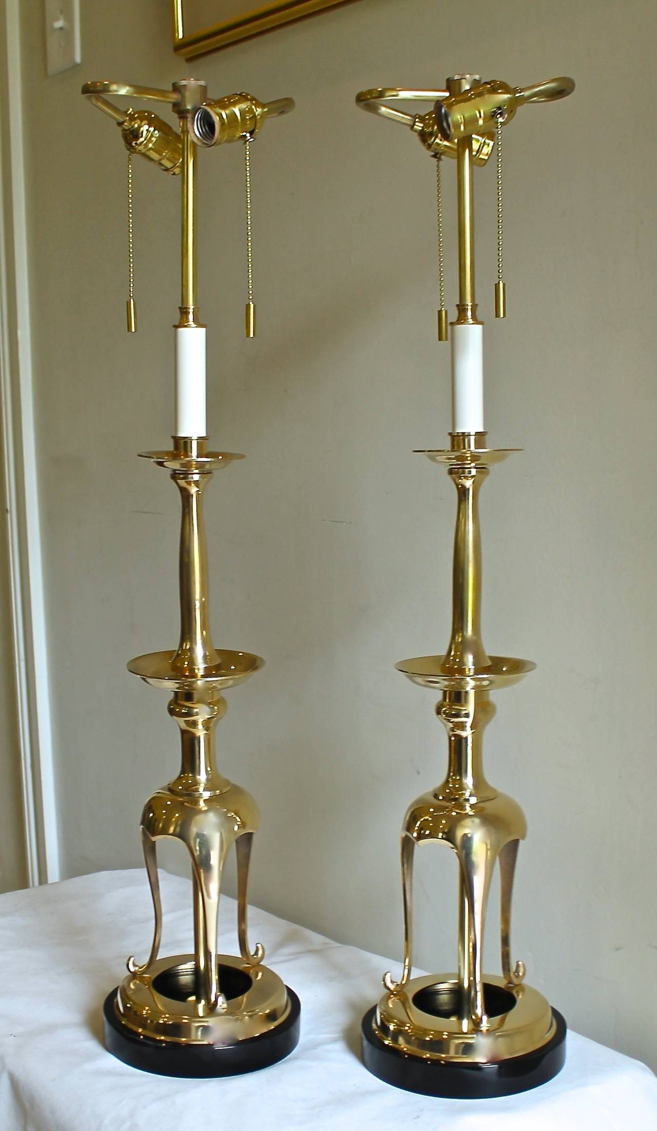 Pair solid brass Asian style candle sticks converted to table lamps resting on black lacquered wood bases. Newly wired with French style rayon covered cords and brass double cluster fittings.