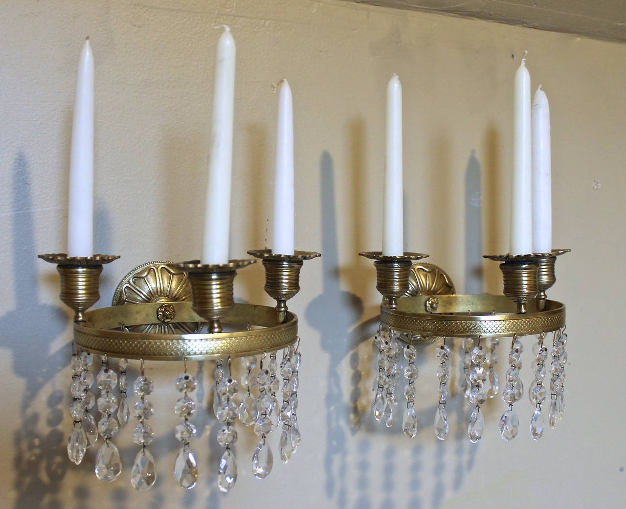 Pair of early French Empire brass and crystal wall sconces with three candle cups and removable drip pans on knurled oval banding mounted to a round backplate. Nicely chased details and patina. Not electrified.