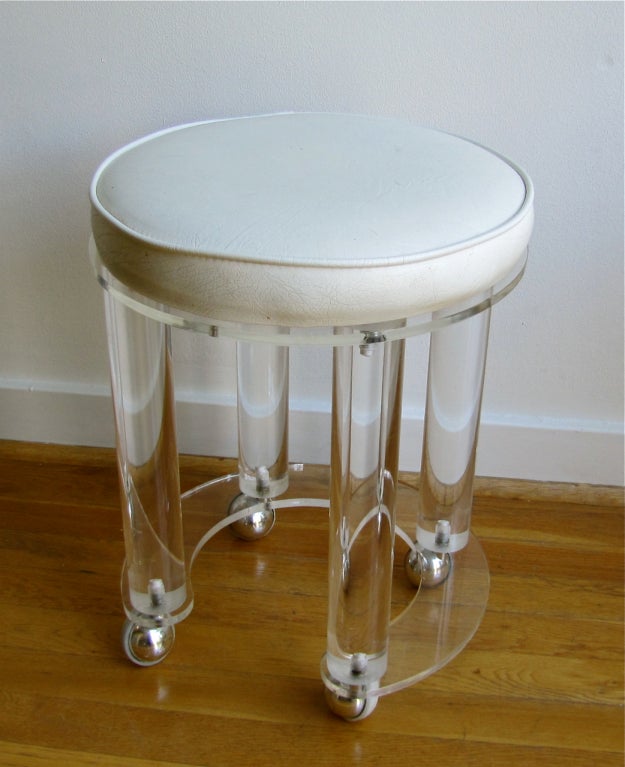 Circular acrylic vanity stool with white faux leather seat and metal casters.