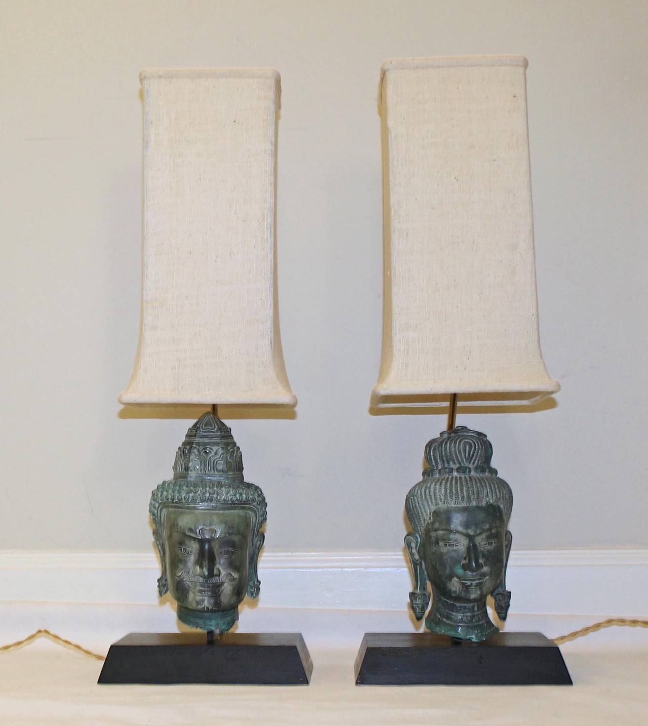Fantastic and rare pair of patinated bronze female and male Burmese Buddha head lamps mounted on wood bases, with original stylized tall shades. Brass fittings, newly wired including French twist cords. 

Measures: Overall height with shade