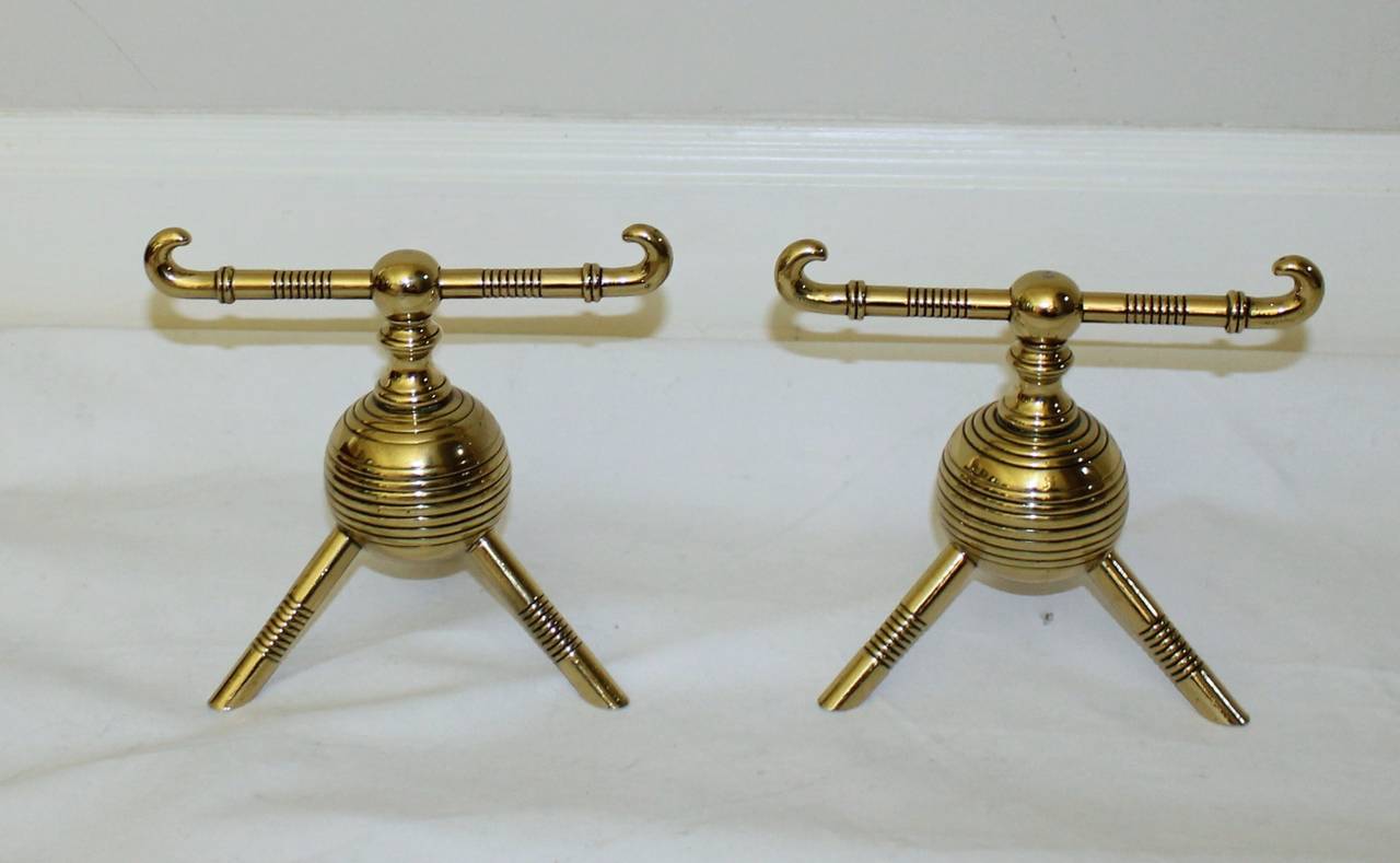 Pair English Aesthetic Movement period brass andirons, attributed Christopher Dresser. Each with ring-turned horizontal bar resting on a bulbous body with tripod feet, stamped 57 and 85 underneath. Brass has more recently been polished &