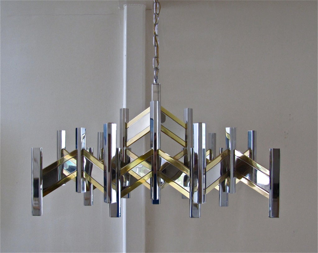 Very large and hard to find chevron zig zag body form chandelier with 21 lights by Gaetano Sciolari. Made of polished chrome and brass. Many scratches to chrome panels, price reflects this. Responsibility of buyer to have polished or replated.