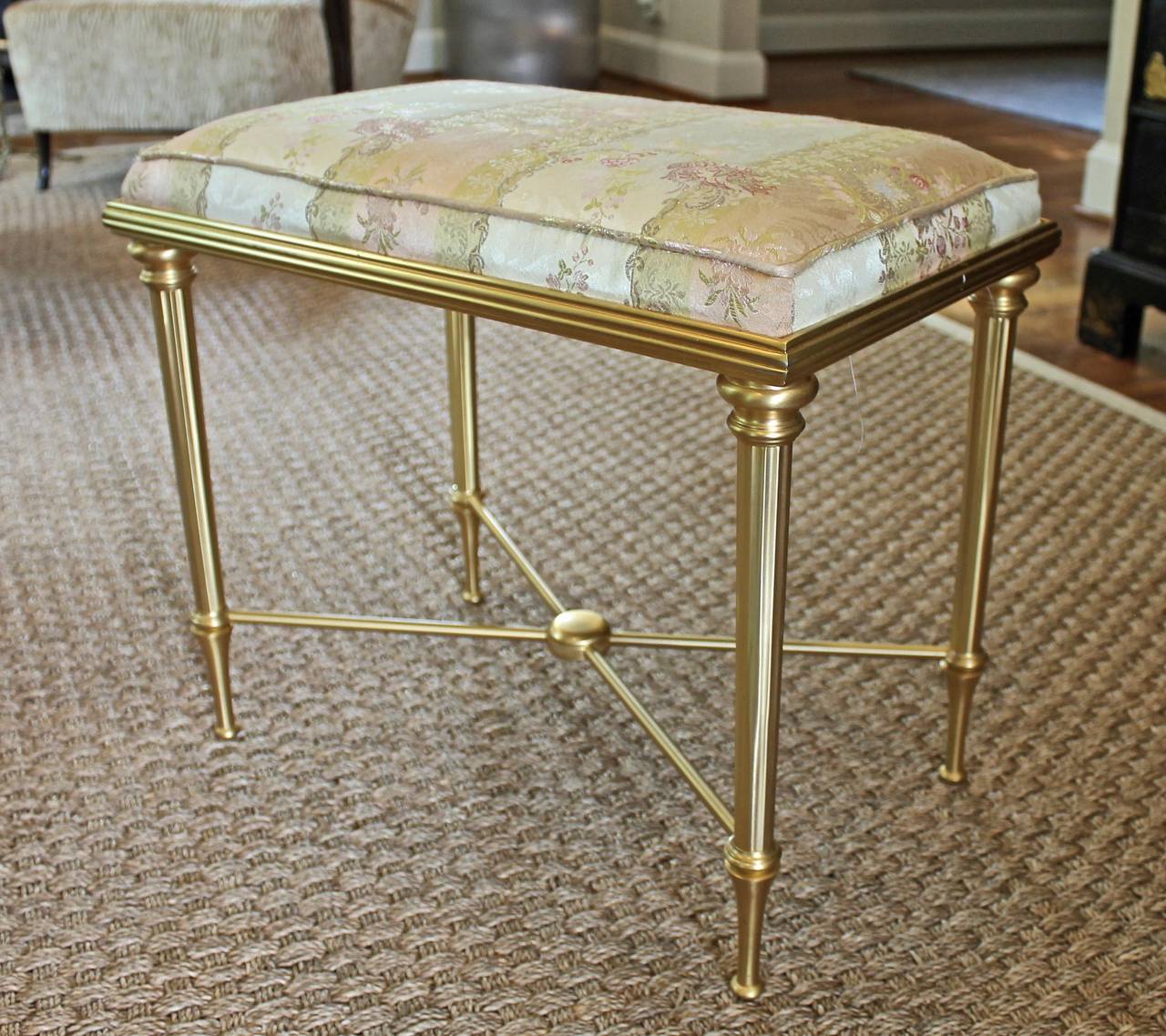 French satin gilt brass x-stretcher bench with upholstered silk lisere cushion top. High quality smaller scale bench with solid sturdy construction.