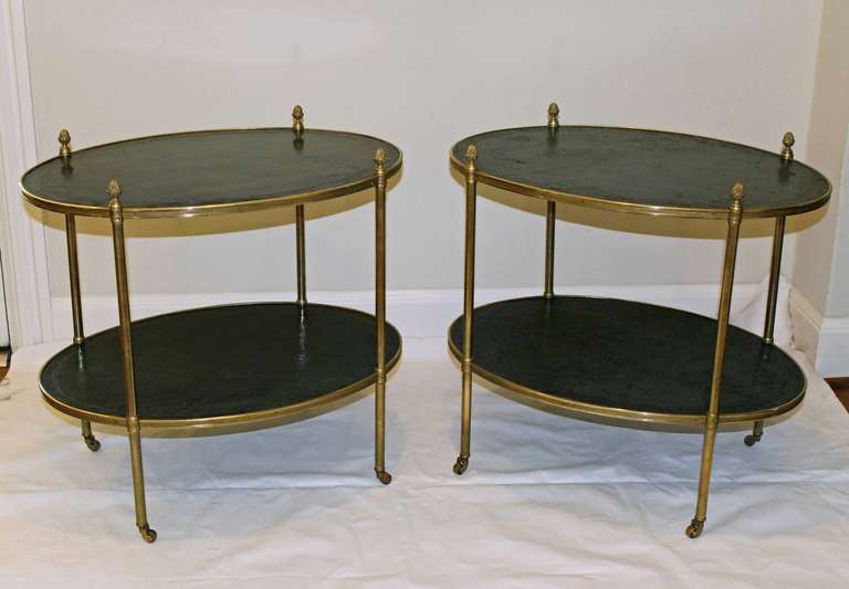 Outstanding pair of Regency style oval two tier brass and dark green leather embossed tops, with casters and intricately chased acorn finials. Height of table top is 21.5
