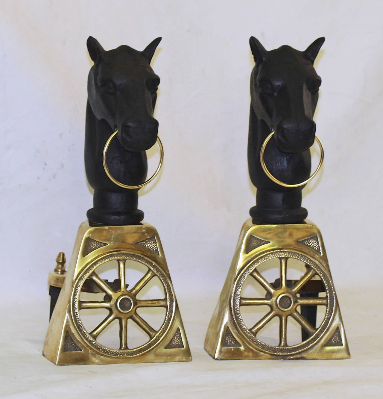 Pair of brass and cast iron andirons with horse head and wagon wheel motif.