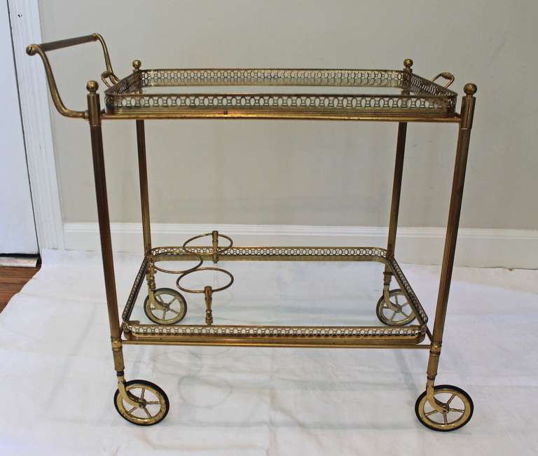 French brass bar cart with two tier glass inset shelves and beverage holder. Nice detailing including reeded legs and solid brass casters. Size: 28.25 overall height to handle, 26