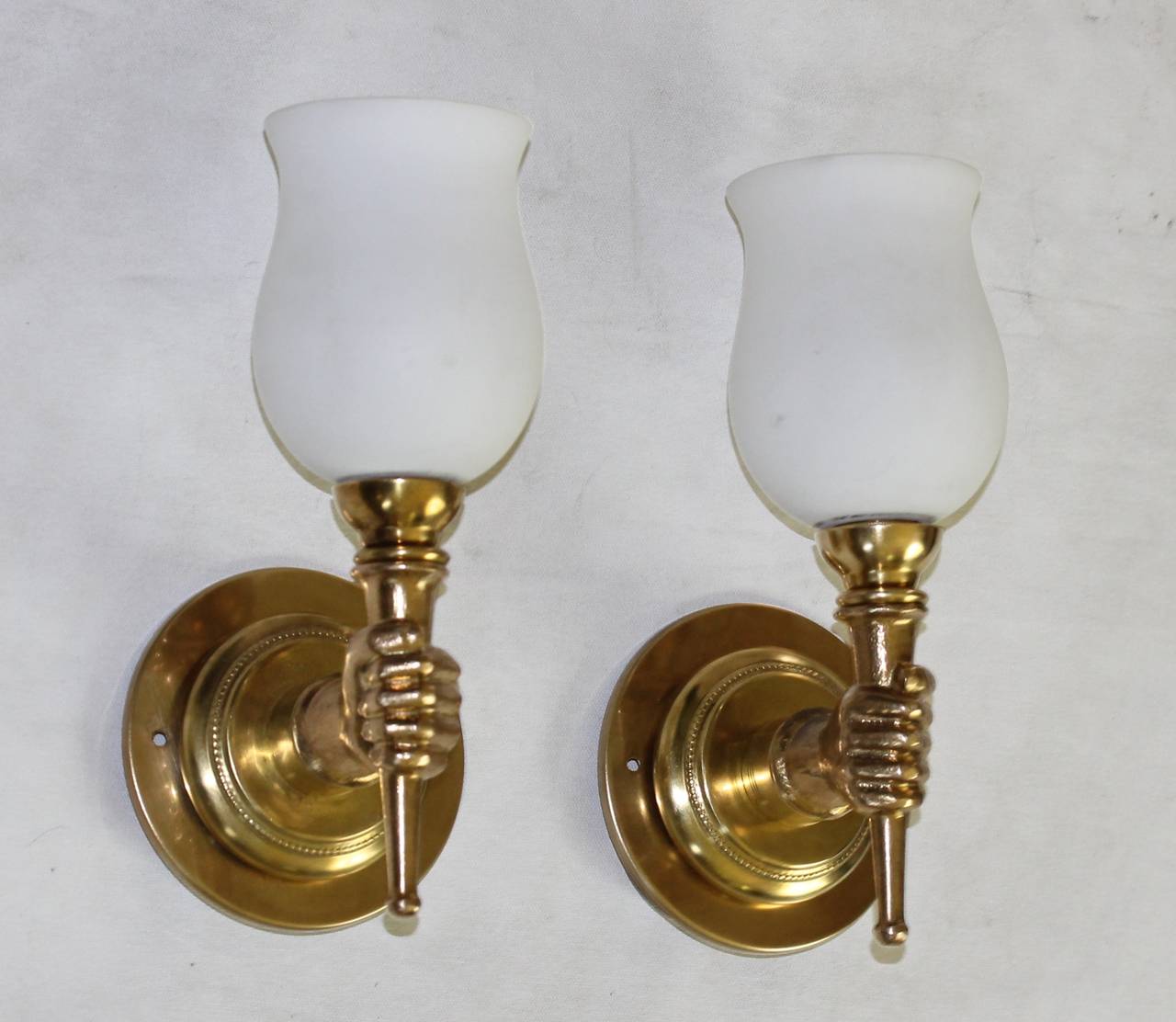 Pair French 1940's bronze or brass wall sconces of hands holding a torch, attributed to John Devoluy. Opaque white glass shades included. Each sconce uses 1 - 40 watt max candelabra base bulb. Newly wired. Height without shade 5