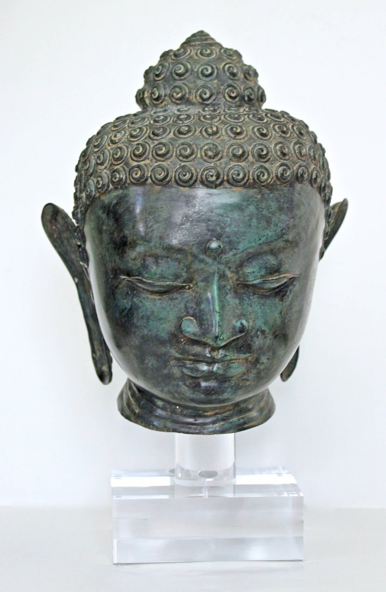Burmese patinated bronze head of Buddha mounted on custom acrylic stand. The youthful face is peaceful and serine framed by elongated ear lobes. A striking art object with fine quality workmanship. Height of head 13