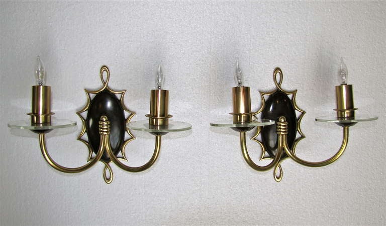 Pair of French Jules Leleu style brass double arm wall sconces with clear glass bobeches. Oval backplates are darkened brass (not paint). Each sconce uses two candelabra base bulbs. Newly wired for US.

Measures: 10