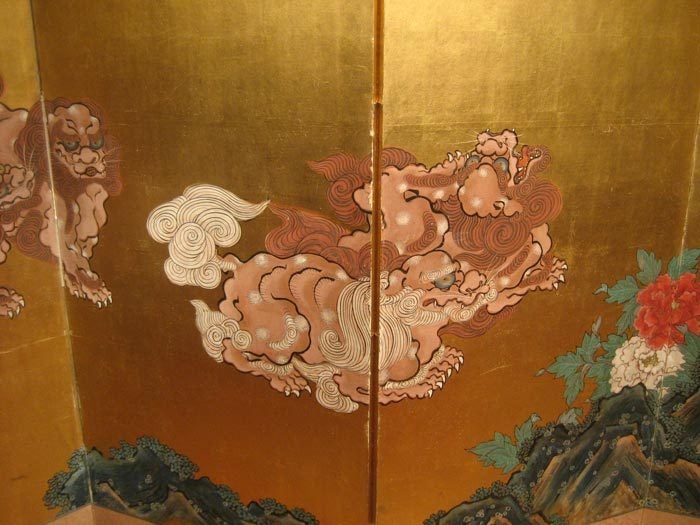 Boldly painted six-panel folding screen (byobu) depicting the classic subject of frolicking mythological Chinese lion dogs, or Shi Shi, amongst peonies on a gold leaf background with embossed signature in lower left corner, with inscription from