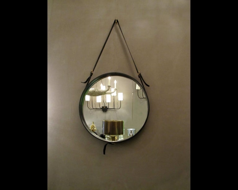 In 1950, the designer Jacques Adnet developped a collection of furniture and accessories for the famous Hermes House. This mirror is derived. It's all round, surrounded by leather straps, connected by brass hinges as belt buckles. The strap allows