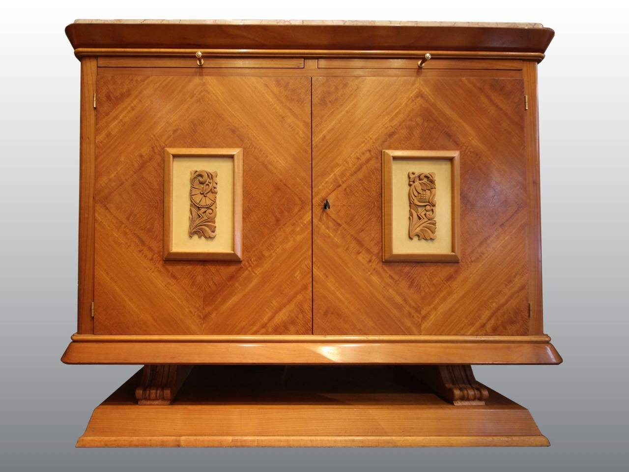 Jolie armoire des années 1940 en sycomore avec deux tirettes. Les portes sont ornées de deux panneaux en bois sculpté. Dessus original en marbre. Intérieur et étagères en placage d'acajou.
