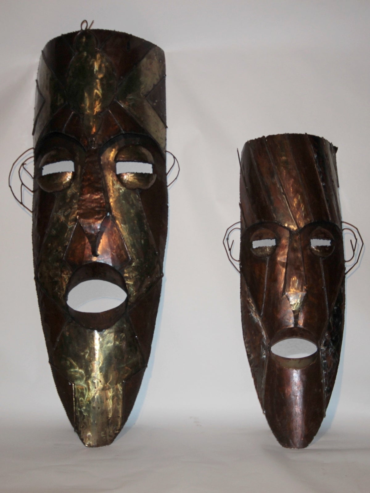 Two 1970s tiki masks, interesting work in three metals, can be used as simple decorations or do extraordinary and very dramatic lighting wall lights.

Dimension of the smallest:
Height: 150 cm. Width: 43 cm and 2 X 7 cm for the two