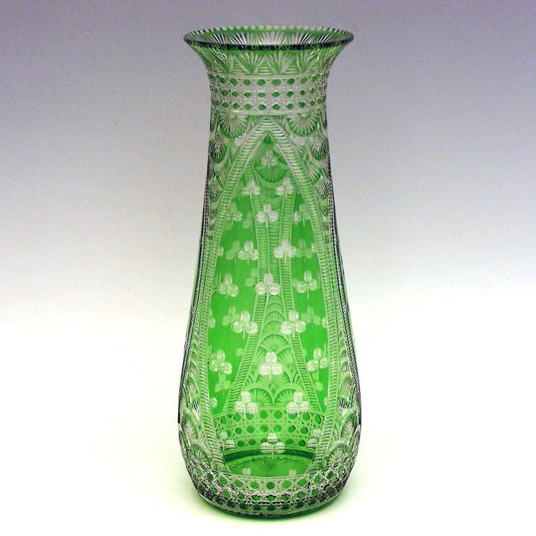 This cut to clear crystal vase in a delicate green is a master work from the renowned English glassworks Stevens and Williams. The delightful shamrock pattern gives us visual rest from the complexity of the ornate fan embellishments and bands of