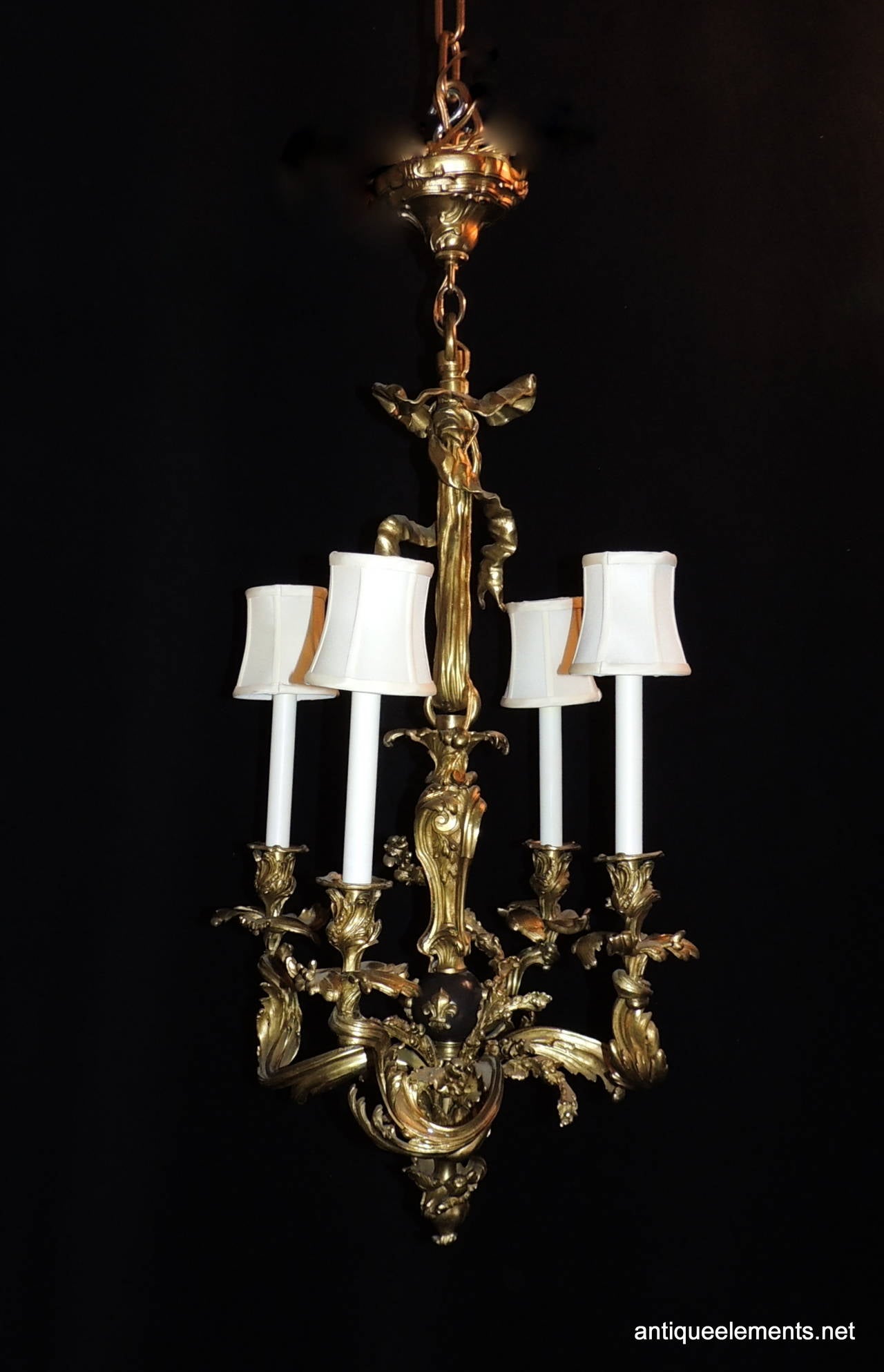 This wonderful doré bronze chandelier with four lights is filled with beautiful swirls of bronze with floral, swag and ribbon detail. At the center is a patina globe accented with fleur-de-lis accents. Finishing this chandelier is a full bow top