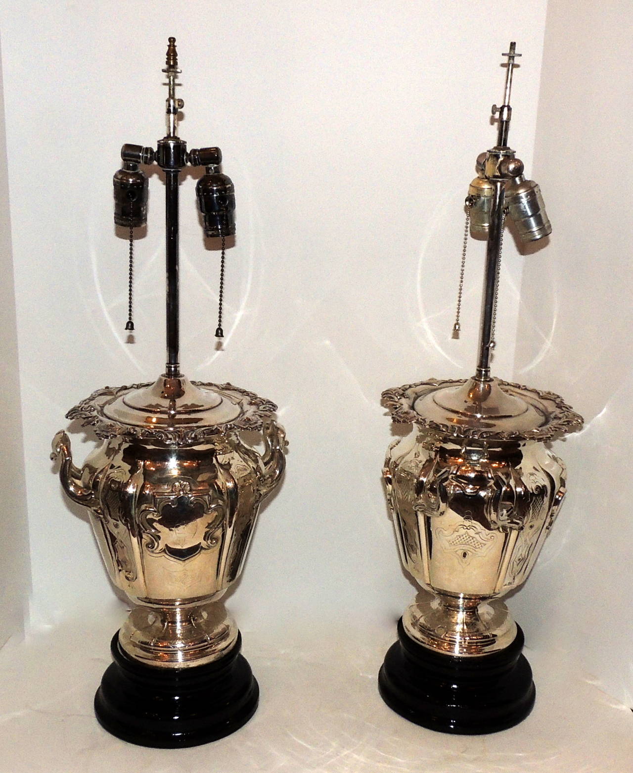 A wonderful unique pair of silver plated lamps with two lights. Appears to have been made from antique silver plated champagne coolers. Beautiful engraved design surrounds the 10" high center, delicately shaped handles and scalloped and