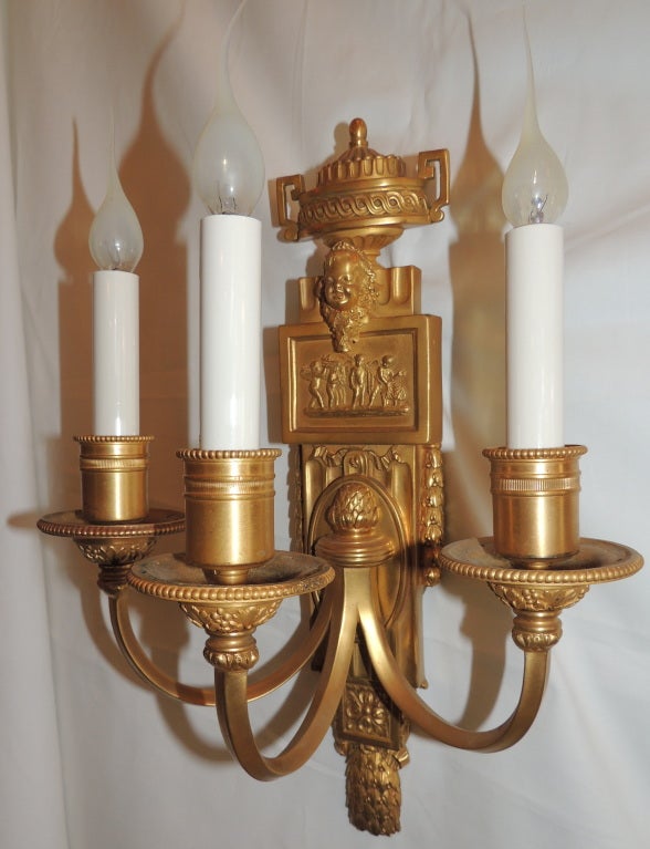 Pair of very fine Caldwell doré bronze three-arm sconces with Cherub plaque and urn top in the neoclassical form.