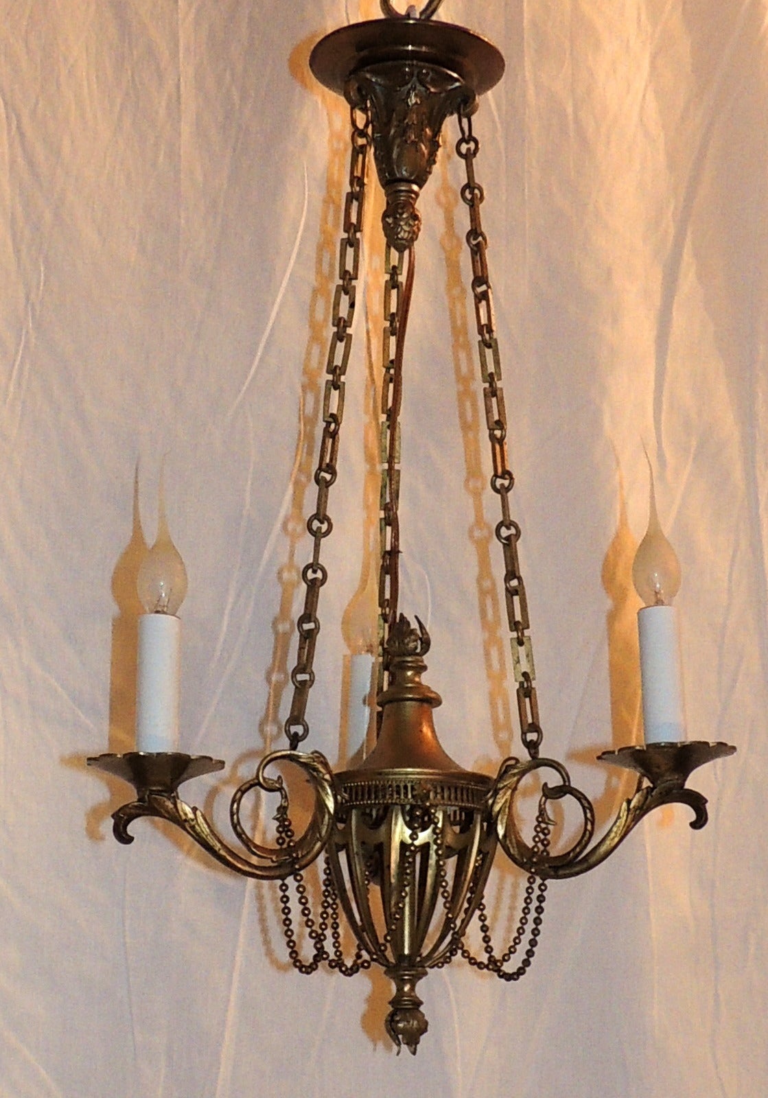 Understated elegance is the best description of this three-arm chandelier.
Beautiful box chain supports the three-scroll and filigree engraved arms supporting the lights. The top and bottom centre are decorated with flame top and bottom detail and