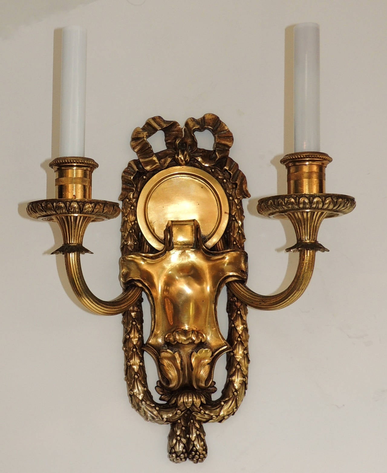 Three pairs of marked Caldwell bronze sconces with embellished bow top and framed with filigree draping. With a softly aged bronze patina, the sconces are set off with a wonderful polished centre, the two fluted arms, floral decorated and beaded