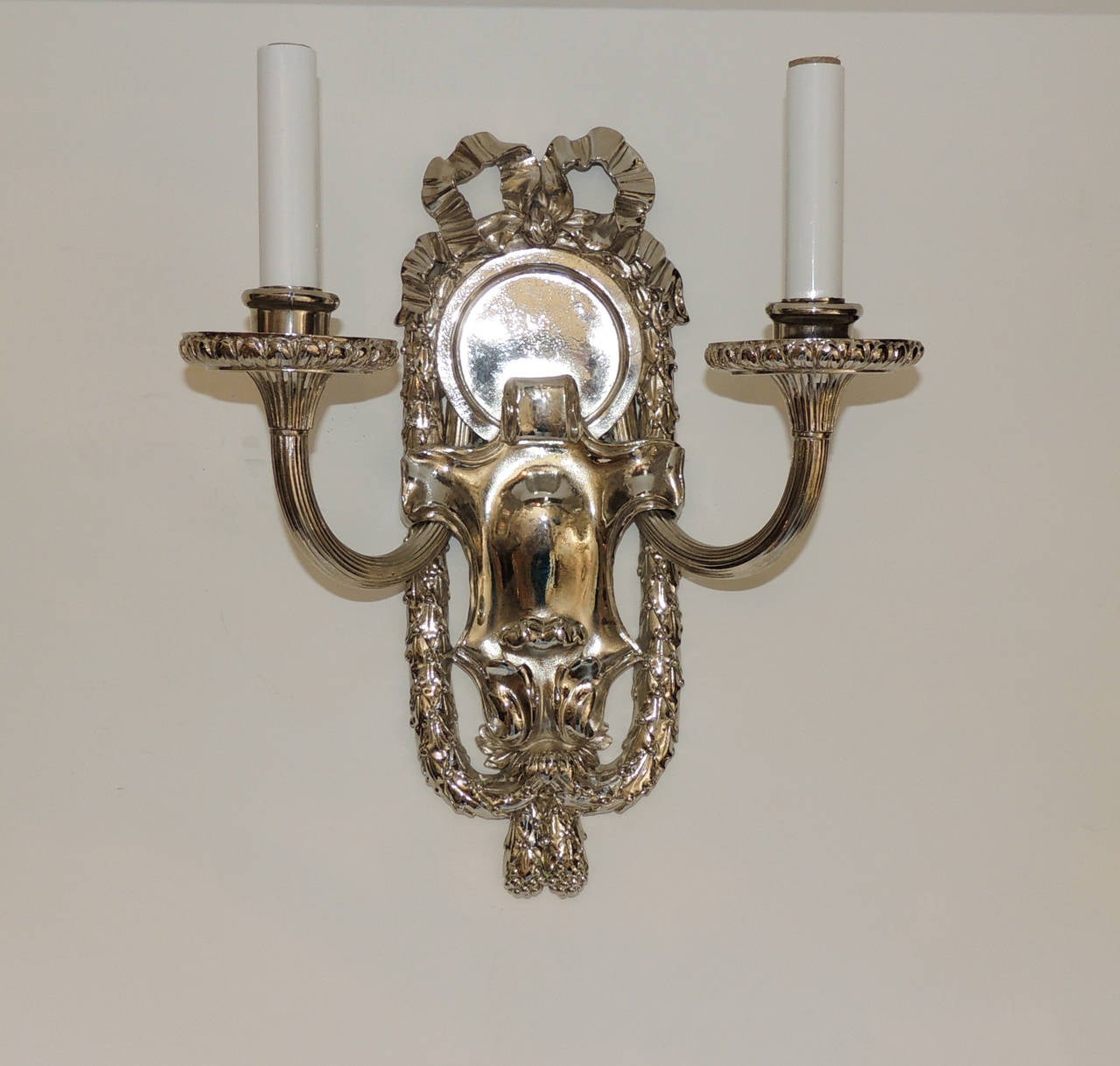 An incredible pair of marked Caldwell sconces with embellished bow top and framed with filigree draping. Set off with a wonderful polished center, the two fluted arms and fluted bobeches are the beautiful finish for these polished nickel