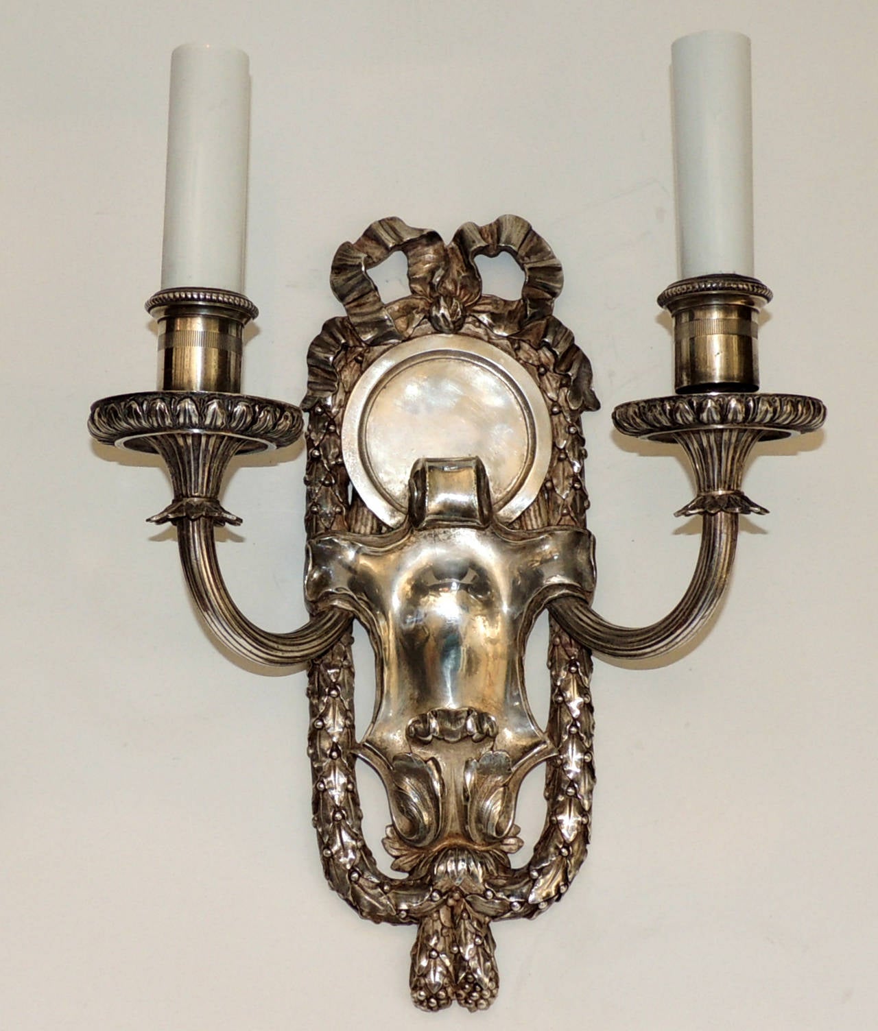 We Have Available Two pairs of marked Caldwell silvered bronze sconces with embellished bow top and framed with filigree draping. With a softly aged silvered bronze patina, the sconces are set off with a wonderful polished center, the two fluted