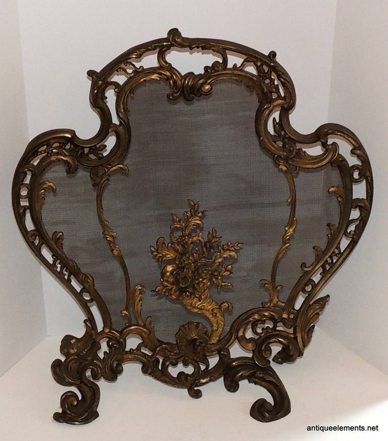 Pierced bronze scrollwork frames these fire place screens with a center floral bouquet. With original screen and a beautiful scroll shape that is detailed throughout the piece including the feet and the flourish along the bottom, this is a Classic