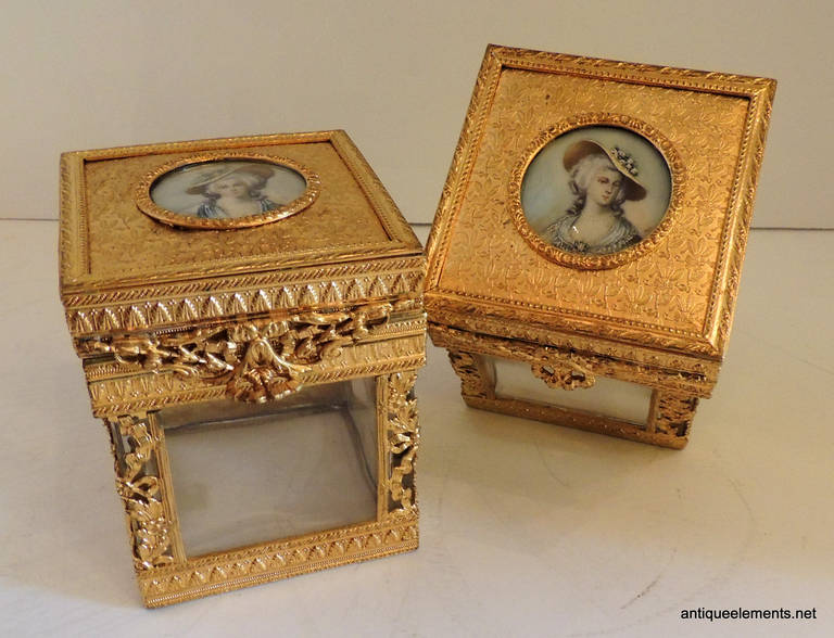 This elegant pair of bronze boxes are decorated with miniature portraits of two elegant ladies and have crystal inserts and mirrors on the box interiors. One of the boxes has a mirror that is stained, the other is in good condition. A beautiful