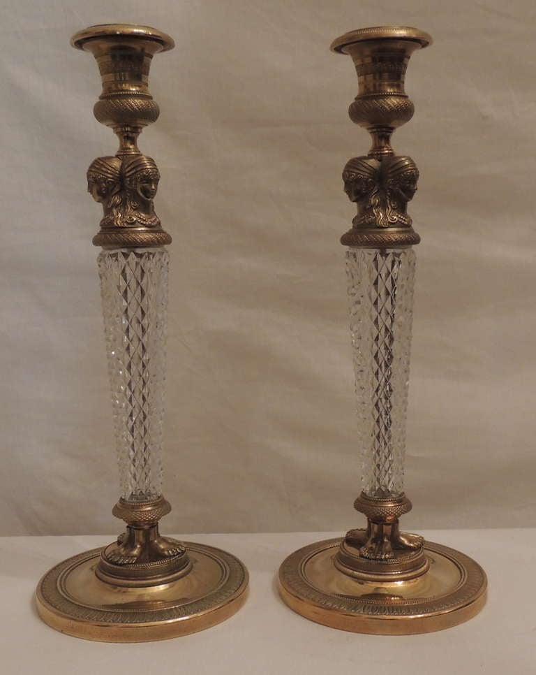 An elegant French Empire or neoclassical pair of doré bronze and cut crystal ormolu-mounted candlesticks.