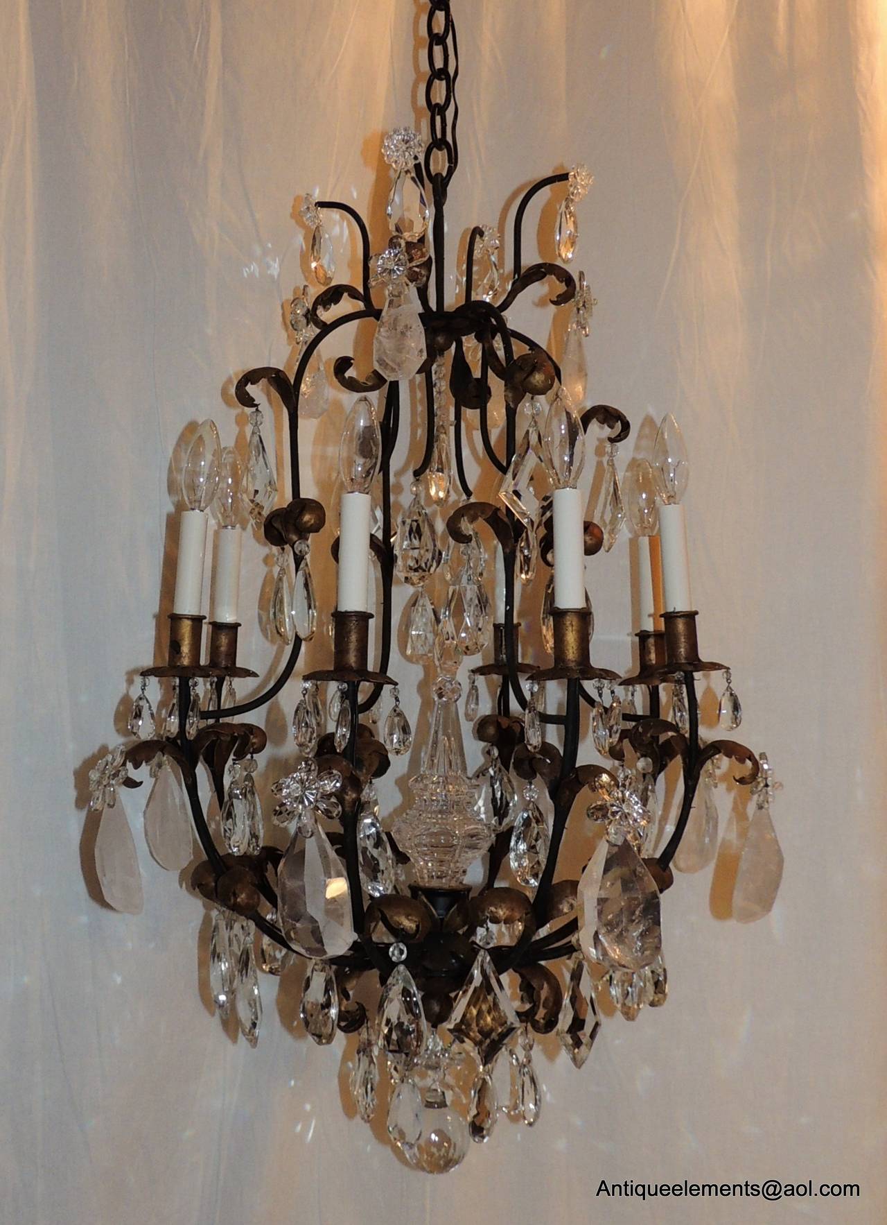 This transitional gilt metal chandelier with eight-lights has wonderful rock crystal prisms, pear shaped and diamond shaped crystal prisms. There is a crystal spire that is in the centre and is topped with a crystal drop from above. Each of the gilt