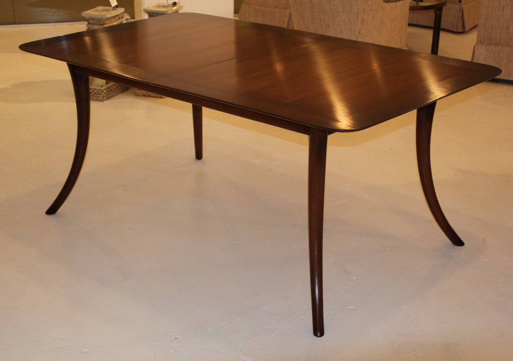 A walnut dining table on sabre legs by T.H. Robsjohn-Gibbings for Widdicomb. Expertly restored and finished in a warm chestnut brown that shades darker at the edges. The table comes with two 18-inch leaves and extends to 104 inches.