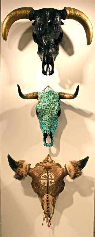 A grouping of hanging bovine skulls – one lacquered black with gilt horns, the other encrusted with turquoise, the third etched and fitted with detachable fur-trimmed horn caps.

black skull: 29