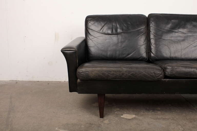 Mid century three seat sofa in original black leather with triangular rosewood legs.