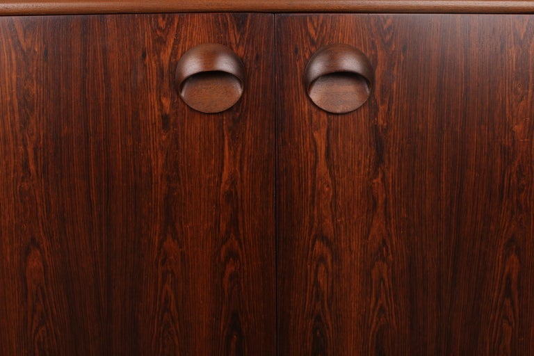 Rosewood mid century modern low, long sideboard by McIntosh of Scotland.  Center section double doors, left side drawer bank and right side drop down bar.