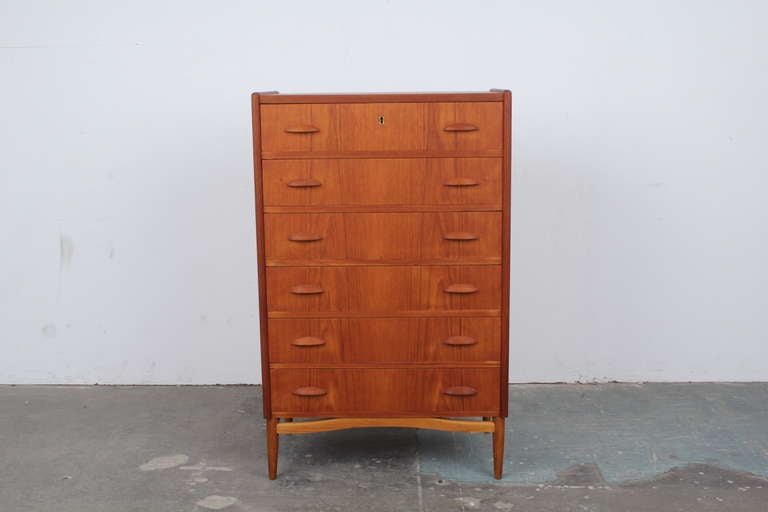 Teak Danish mid century modern tall boy dresser with six pull out drawers and one locking top drawer. Unique articulated leg base.