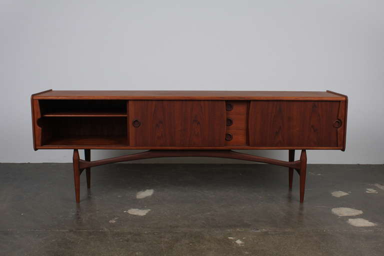 Beautiful and rare mid century modern Danish low teak sideboard with 2 sliding doors, 3 drawers and a sculptural arching base with rounded cut out handles.