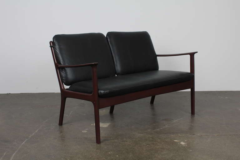 Petite Danish Mid-Century Modern love seat by Ole Wanscher with a solid mahogany wood frame. Newly upholstered in black leather, newly refinished in lacquer.