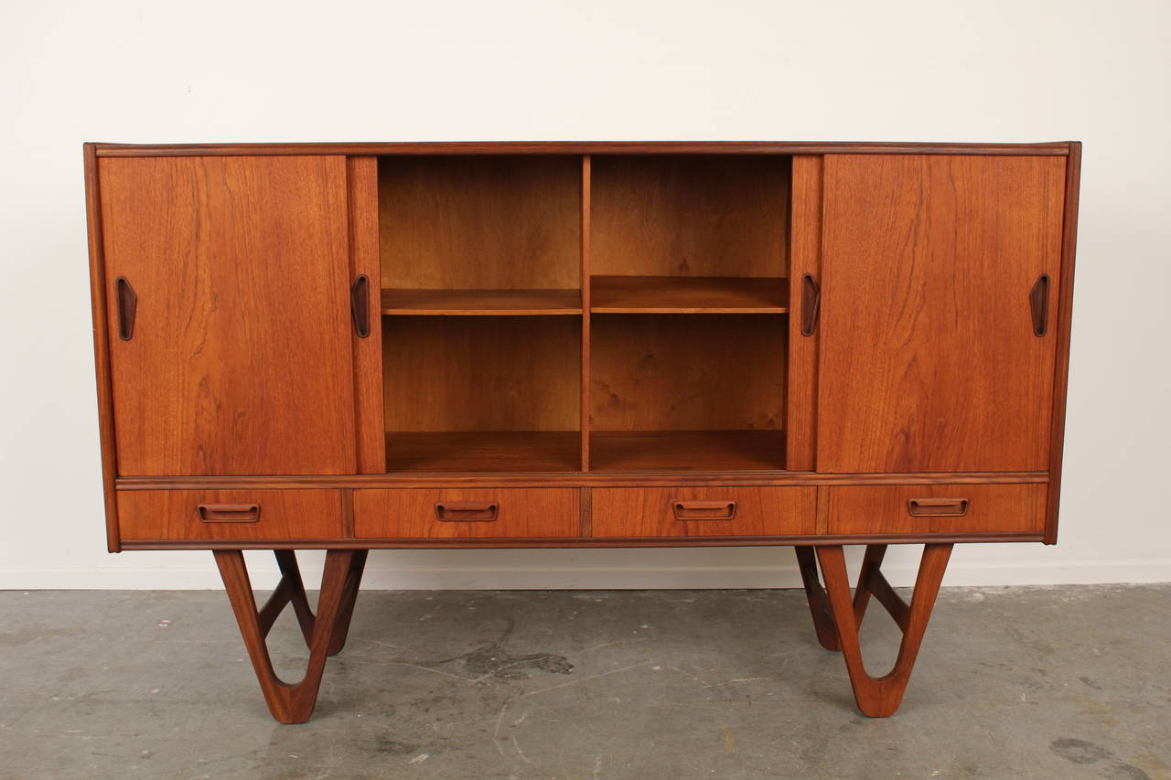 Stunning vintage teak credenza or tall sideboard made in Denmark.  Gorgeous wood hairpin legs, carved drawer and door handles with interior shelves.  Beautiful grain and completely refinished.  Really unique, handsome, and functional piece.