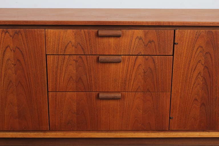 English mid century modern teak sideboard with stunning grain patterns and unique tubular door and drawer handles. Made by Austin Suite of England.