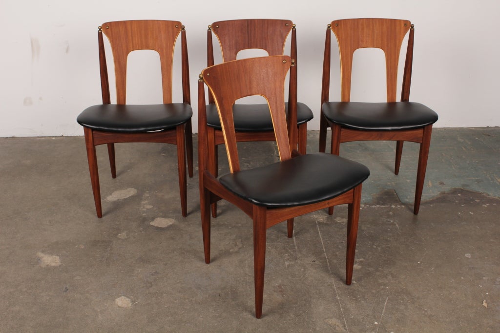 English mid century modern cut-out, angled back teak dining chairs with brass hardware, newly refinished and upholstered in black vinyl.