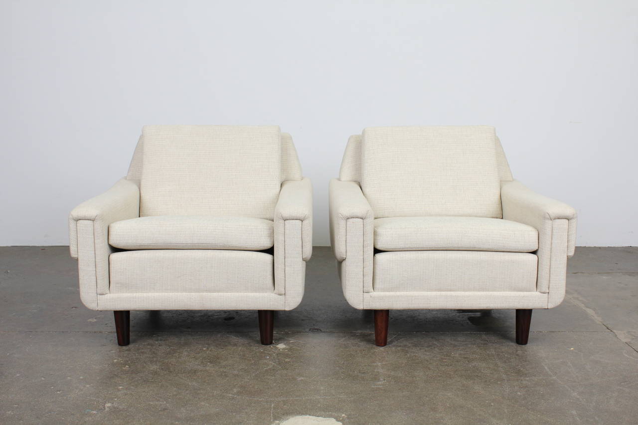 A pair of Danish mid century modern low lounge chairs with angular detailed arms, newly upholstered in a creme colored woven fabric, with solid rosewood legs.