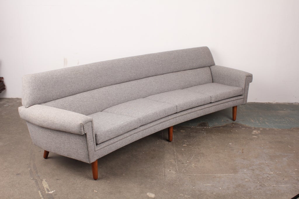 Newly upholstered mid century modern Danish 4 seat curved sofa.  Tie back with 4 loose seat cushions, lower lumbar back support as well.  Upholstered in grey fabric with beautiful lines accentuated by the fabric.  Teak legs.