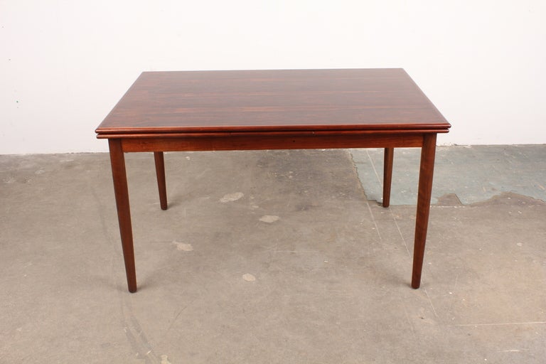 Mid century modern Rosewood dining table with two pull out draw leafs. Large surface area make this a perfect table for entertaining.  Excellent grain throughout the table, with classic Danish tapering round legs.