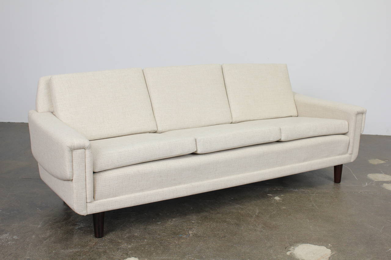 Classically styled Danish Mid-Century sofa upholstered in a sublime cream fabric, with tapering solid rosewood legs. The seat cushions sit on a platform on top of the base, giving this sofa a more plush look.
