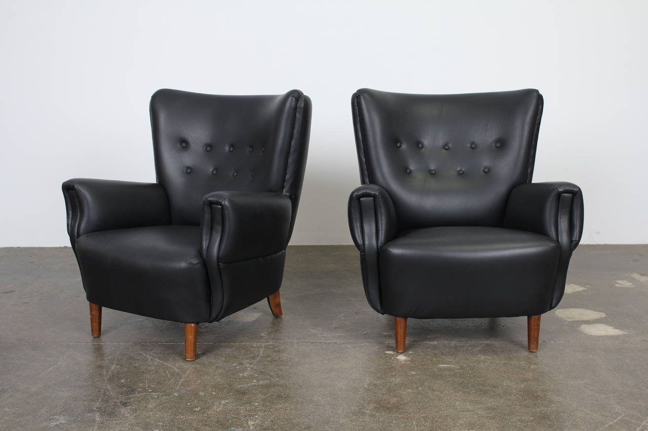 Pair of Danish modern lounge chairs in black leather with tufted, tall barrel backs and padded arms. Newly upholstered in black leather with new foam.