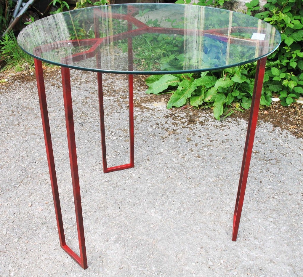 A significant Royere table of red square section steel with circular glass top with polished edge