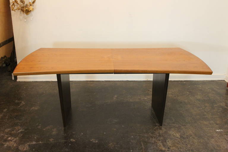 A teak dining table with a bow-shaped top over tapered mahogany slab legs with brass runners, by Harvey Probber Inc.
Table includes two 18