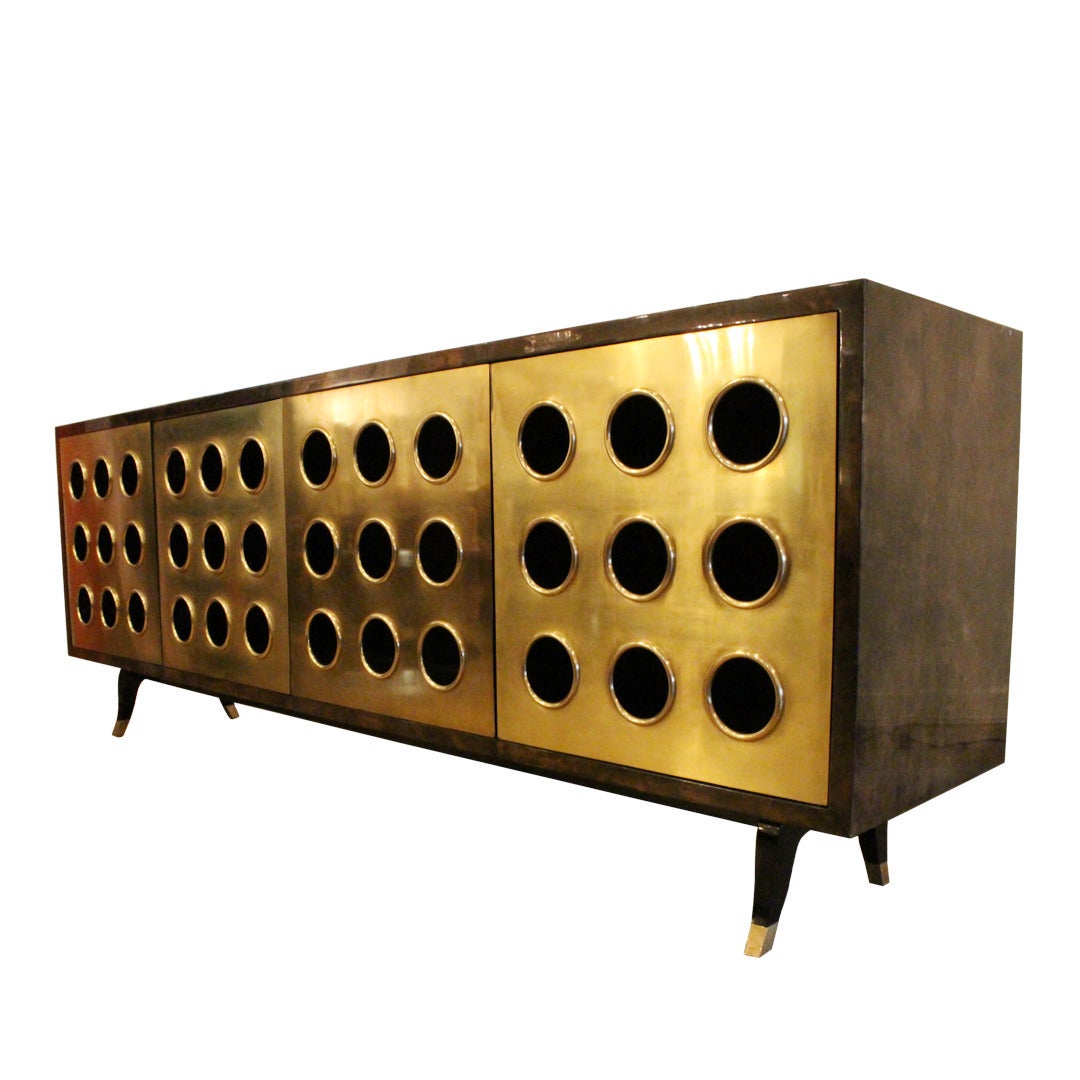 Monumental brass front credenza by Scala Luxury. This piece offers four door with three compartments of storage. The doors are constructed of brass and accented with circular cutouts. The finish on the credenza is in a deep tortoise finish.