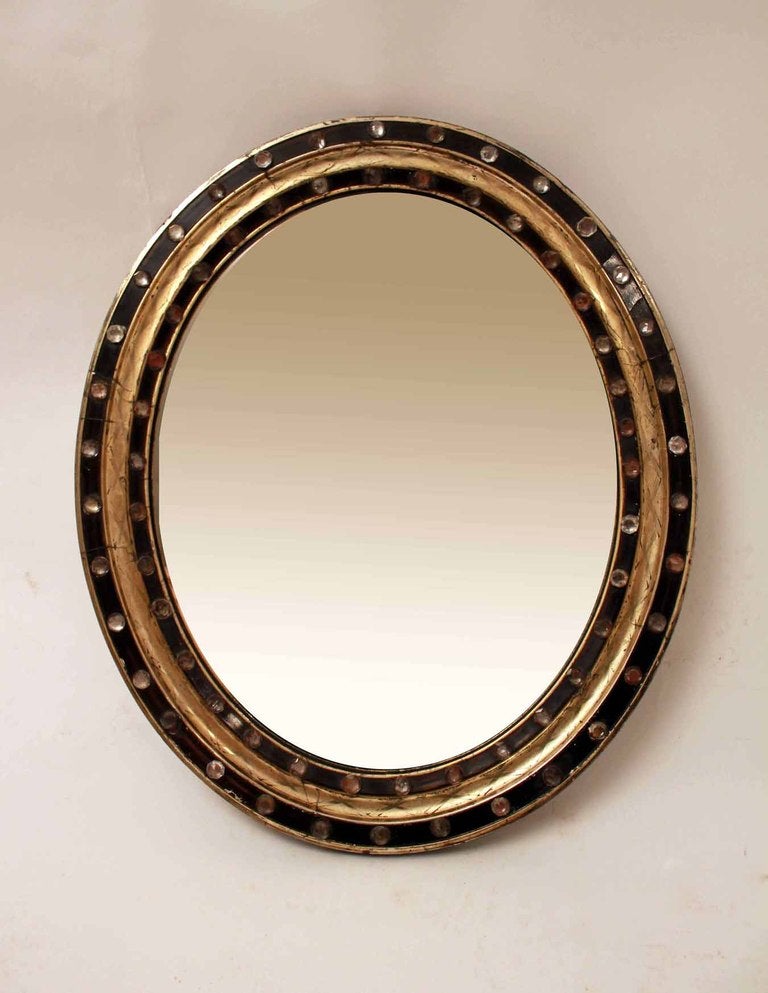 An early 19th century Irish Galway mirror.  Original oval mirror plate within concentric bands, ebonised and gilt.  The outer and inner bands with applied facetted glass studs. 