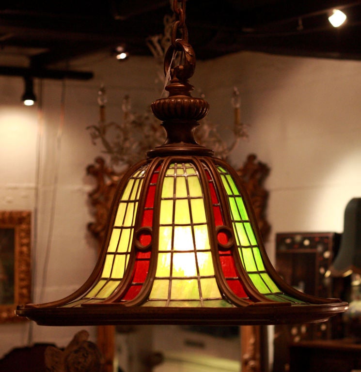 Bronze and leaded glass Arts and Crafts period hanging chandelier in excellent condition.  Red and green stained glass adorn this bell-shaped form, with 